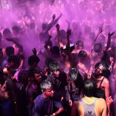 Indian revellers covered in coloured powder dance during 