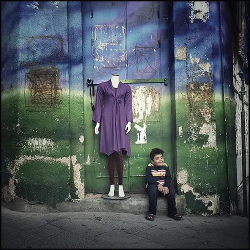 A kid sits beside a mannequin on a sidewalk. Tabriz, East