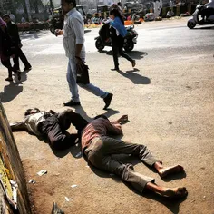 Indian pedestrians walk past two drunk men lying on a str
