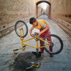 A boy tries to repair his bike in front of his house whic