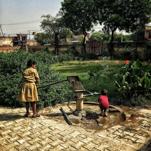 An Indian girl helps her brother drink water from a hand 