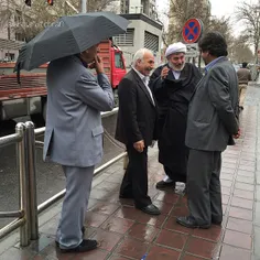 Middle-aged coworkers chat under the rain. Mirdamad Ave. 