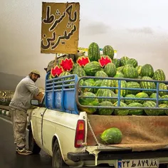 A man selling watermelons at the side of a road. The sign