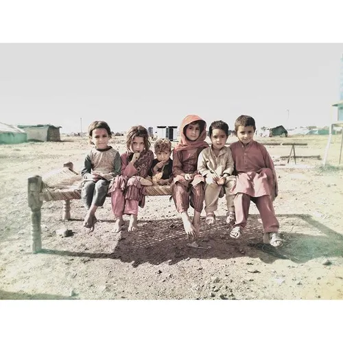 A group of children sit on a chaar pai at a camp for Inte
