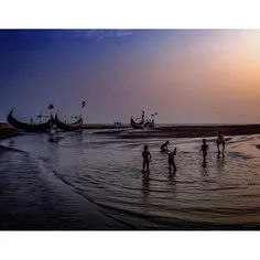 The sunsets behind boys playing in the tide in Coxs Bazar