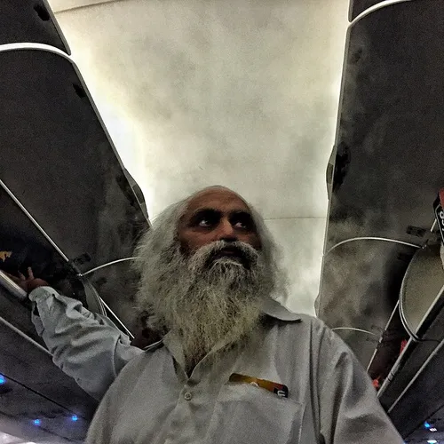 An Indian elderly man looks for space for his luggage ins