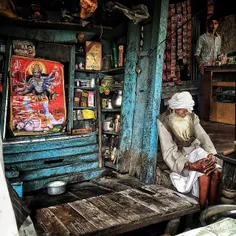 An Indian elderly person sits at his roadside makeshift t