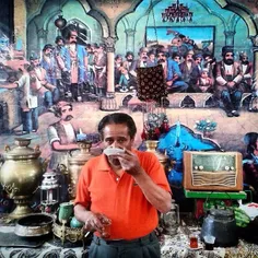 A man drinks tea at a traditional café. The mural in the 