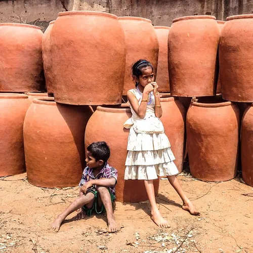 A boy and girl lean against clay pots in a workshop outsi