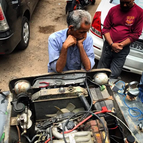 Indian mechanics stand near a broken jeep as they wait fo