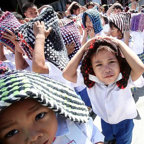 Students use rugs for cover during an earthquake drill in