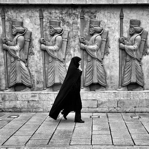 A woman walks by a wall on which the patterns of Achaemen