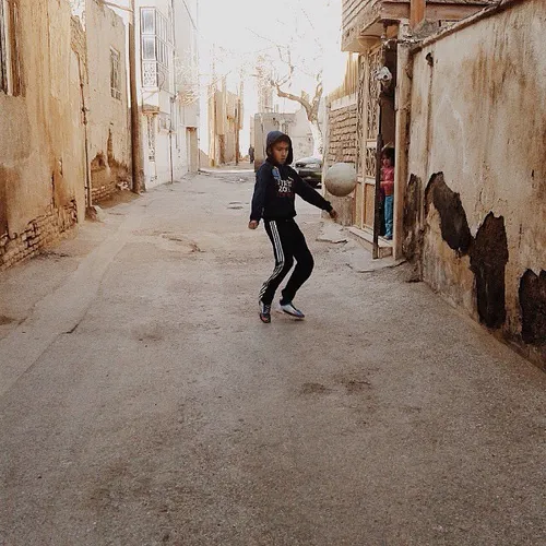 A boy plays with a ball in a narrow alley. Mashhad, Razav