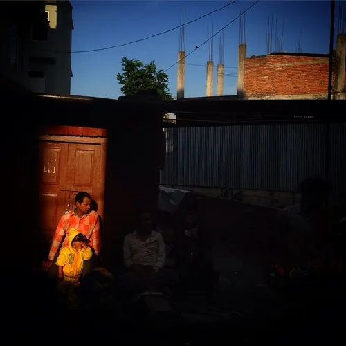 A Nepalese man sits down with his son in a pocket of ligh