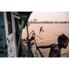 Kids jump off of an abandoned boat into the Yangon River.