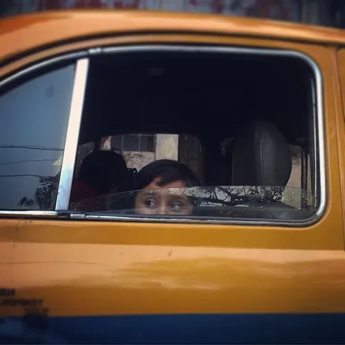 A child looks out of the window of a yellow ambassador ca