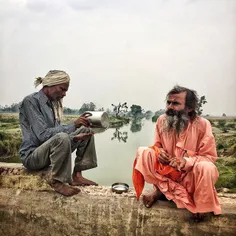 An Indian man sits with a Sadhu (Hindu Saint) on a platfo