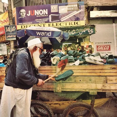 An elderly man seeing dusting the shoes that are for sale