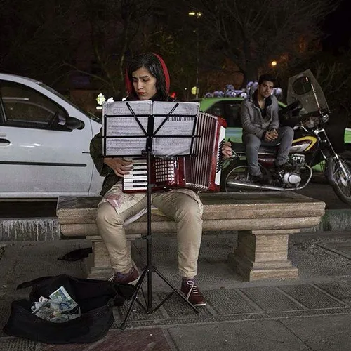 A woman plays the accordions at the side of a street. Teh