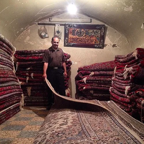Shopkeeper shows customers handmade carpets. Qazvin, Iran