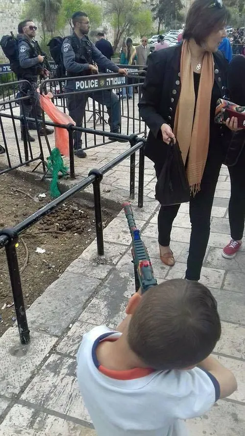 کودک فلسطینی که تفنگ اسباب بازی خود را روبروی در عامود به
