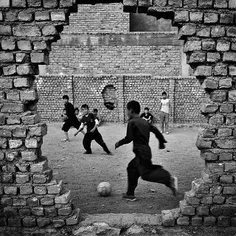 Children play football within the ruins of a playground i