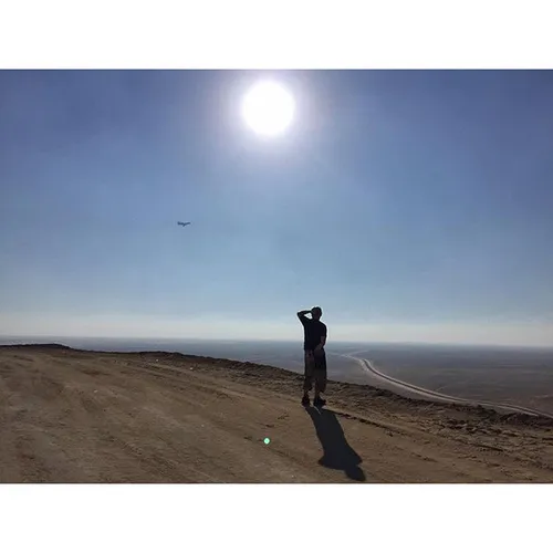 A man surveys the desert from a man-made hill as a plane 