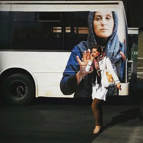 A woman passes by a public bus on which a movie ad is dra