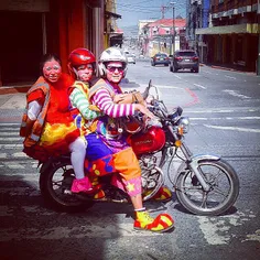 Three people on a motorcycle dressed as clowns in downtow