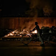 A vegetable vendor drags his trolley past the fire set up