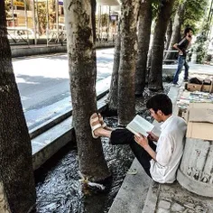 A man reads a book on a sidewalk. #Tehran, #Iran. Photo b