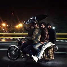 Four young men on a motorcycle,  during a rainy night in 