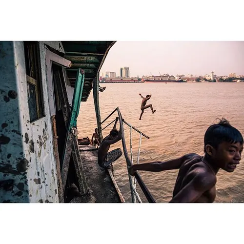 Kids jump off of an abandoned boat into the Yangon River.