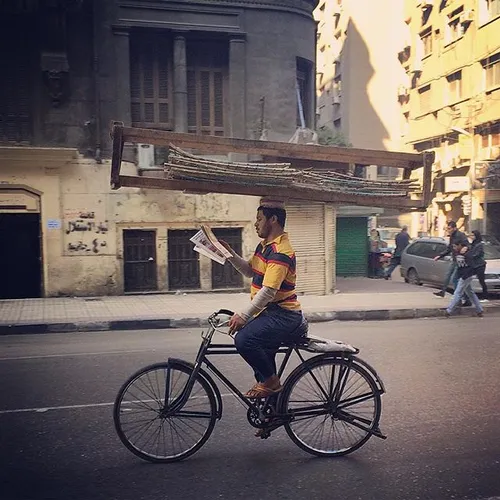 A man reading a newspaper while riding a bicycle and hold