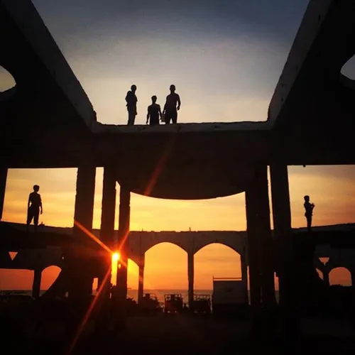 Young men watch the sunset from above a destroyed buildin