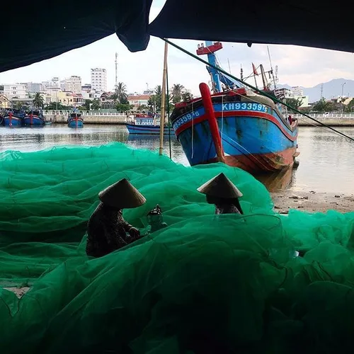 Two woman sewing a giant fishing net in a small hamlet ne