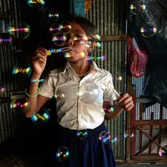 A Cambodian girl blows water bubbles in her house after c