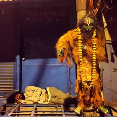An Indian man sleeps beside the effigy of Hindu demon god